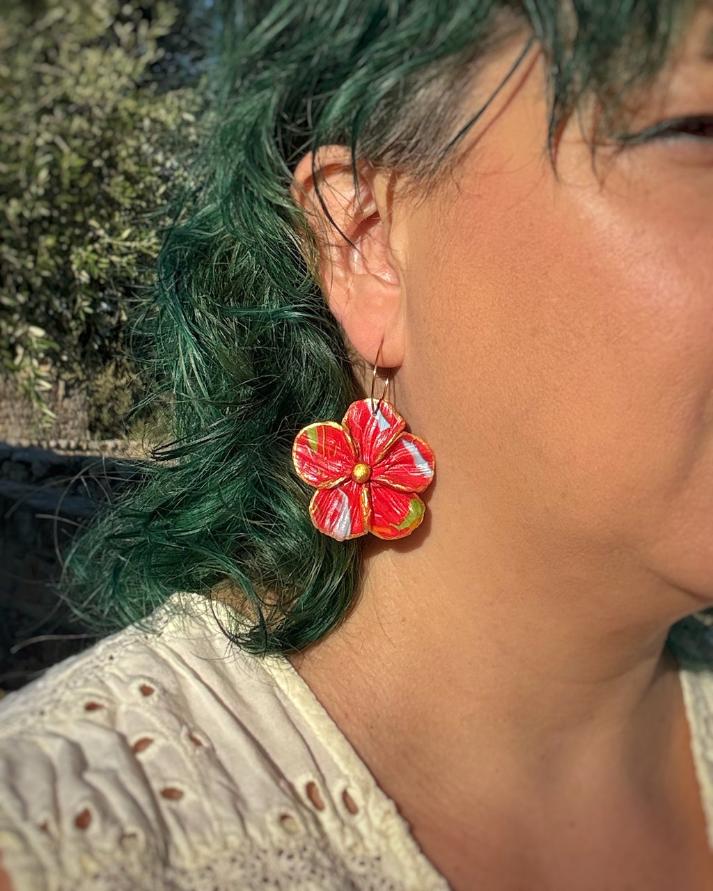 Pendientes Granadilla en tonos rojos sobre modelo . Un diseño floral en aro 