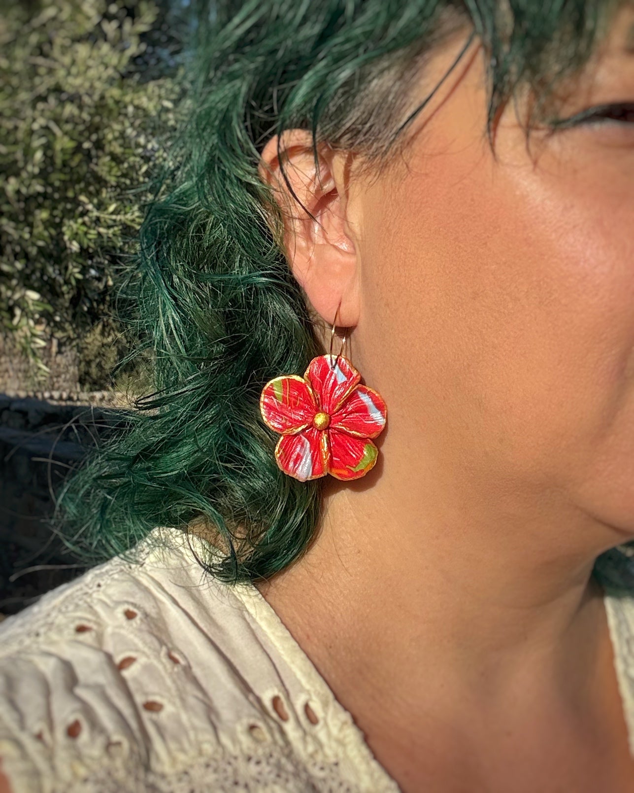 Pendientes Granadilla en tonos rojos sobre modelo . Un diseño floral en aro 